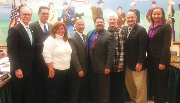 PERTH AMBOY - Councilman Kenneth Gonzalez poses for a photo at his last Council Meeting 12/10/14 (L to R) City Attorney Mark Blunda, Councilman Fernando Irizarry, City Clerk Elaine Jasko, Council President Joel Pabon, Councilman Kenneth Gonzalez, Councilwoman Lisa Nanton, Councilman William Petrick, Business Administrator Jillian Barrick. *Photo by Carolyn Maxwell