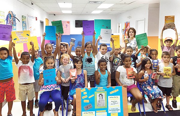PERTH AMBOY - Perth Amboy Mayor Wilda Diaz (back row, right side) and students from I Excel Child Care Center at 165 Washington Street hold signs and food items to remind everyone to attend the City’s “Block Party with a Purpose” on Saturday, August 27 beginning at 11 a.m. The community can celebrate together and donate non-perishable food items to help restock the shelves of the City’s food pantries. Adults and children of all ages are invited to New Brunswick Avenue, between Madison and Maple Streets, for the “Block Party with a Purpose” that includes free hot dogs, inflatable slides and rides, a balloon artist and performances by dance groups. Perth Amboy’s C-Town Supermarket, Quisqueya Foodmarket, Supremo Supermarket and Tropical Supermarket are giving the food drive a big boost by donating products. The “Block Party” is sponsored by the Perth Amboy Business Improvement District (BID), the City’s Recreation Department, Renovation House, Lighthouse Worship Center, and the St. Vincent de Paul Food Pantry. *Photo by the Perth Amboy BID