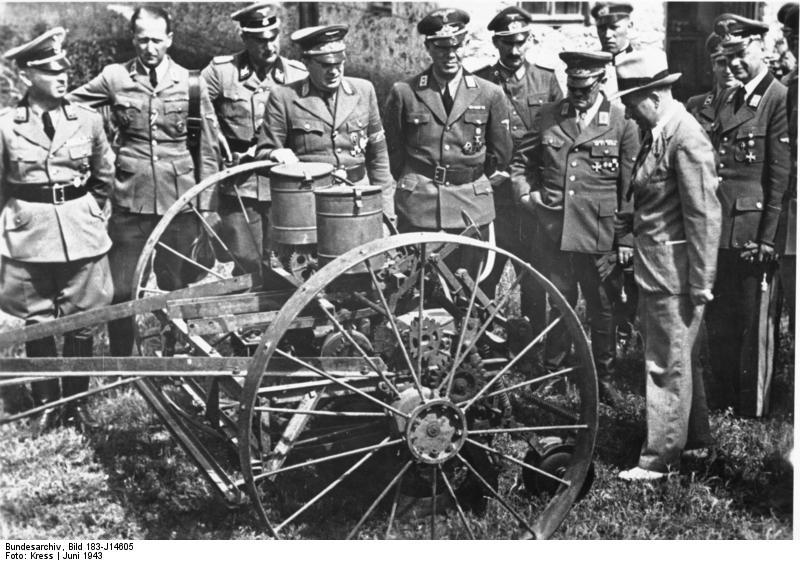 The following is the English translation of the German caption for this picture: Ukraine, visit of Rosenberg to Koch. Just last month, the National Minister for the occupied East Territory National Leader Alfred Rosenberg took a business trip through the Ukraine, to inspect the development projects of the National Commission for the Ukraine. This picture shows National Minister Rosenberg at an inspection of new machinery at an agricultural enterprise. To the left of him is National Commissioner Party Leader Koch, General Commissioner Claus Selzner, and Party Leader Dr. Helmuth. Wikimedia Commons.